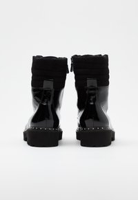 Bottes courtes en cuir verni noir avec dessus en tissu noir matelassé, semelle épaisse et clous en métal le long de la base. Fermeture éclair à l'arrière.