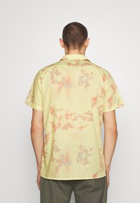 Korte mouwen shirt van lichtgele stof met een bloemenpatroon in vervaagd oranje en blauw, voorzien van een standaard kraag en een relaxte pasvorm.