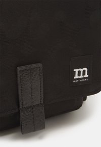 Black textile bag with subtle patterned texture, featuring a tab closure and a woven label with the logo “marimekko” in white.