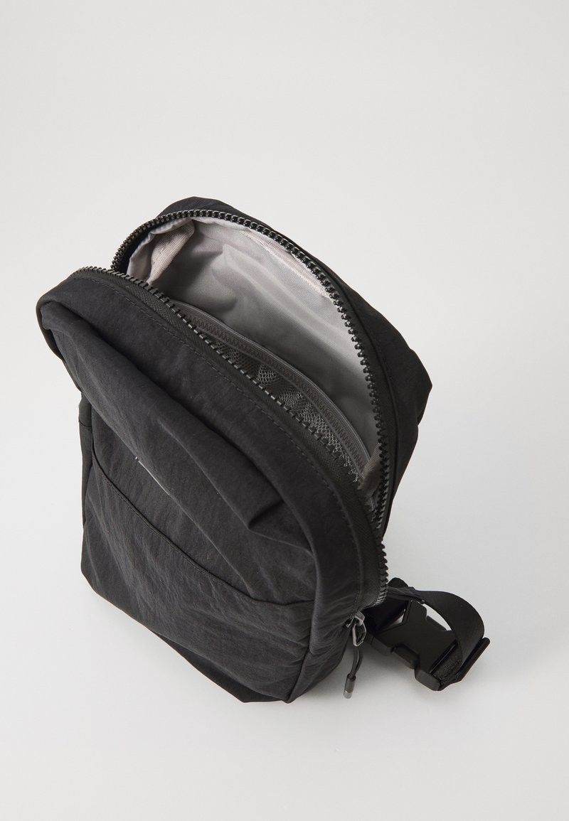 Schwarzer Rucksack mit strukturiertem Finish, ausgestattet mit einem oberen Reißverschluss und einem seitlichen Schnallenriemen. Innen mit grauem Stoff ausgekleidet und einer Netztasche.