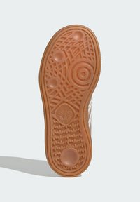 Semelle de chaussure en caoutchouc avec un motif texturé, présentant des motifs circulaires et le logo Adidas ; couleur brun clair avec des rainures pour l'adhérence.