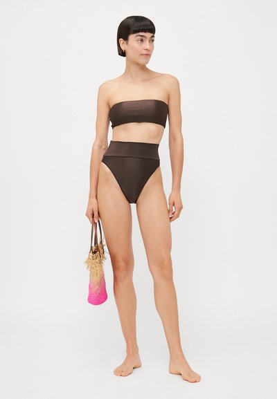 Brūns bikini komplekts ar bezplecu topu un augsta jostaslāņa apakšdaļu. Modelis tur rozā austu somu ar teksturētu apdari.