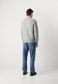 Light gray knitted sweater with ribbed texture, loose fit, and crew neckline, paired with blue jeans and black shoes.