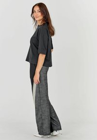 Tricou oversized negru cu mâneci scurte, asortat cu pantaloni largi cu tartan, care au un accent de dungi verticale pe o parte.