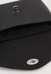 Svart texturerad läderklutch med magnetstängning. Interiören har slät svart tyg. Inkluderar en silverringdetalj.