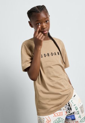 T-shirt a maniche corte color ecrù con la scritta "JORDAN" stampata in nero, caratterizzato da una vestibilità rilassata. Il modello lo abbina a leggings con motivi.