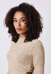 Camicia beige a maniche lunghe con texture a costine e lati arricciati, caratterizzata da un piccolo logo ricamato nella zona del petto.