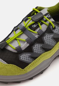 Melnas un pelēkas sporta kurpes ar zaļiem akcentiem, ar teksturētu auduma augšdaļu, elastīgām auklām un izturīgu zoli, kas paredzēta saķerei.