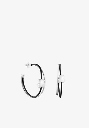 Boucles d’oreilles créoles en argent avec des accents noirs et un petit charme trèfle à quatre feuilles en argent poli sur chaque créole.