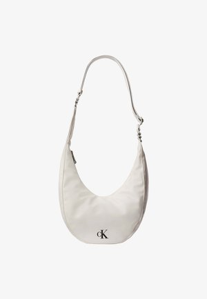 Bolso de hombro de cuero blanco en forma de media luna, con correa ajustable, cierre de cremallera y logotipo negro de Calvin Klein en el frente.