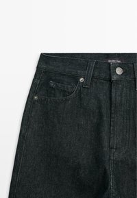 Jeans in denim scuro con vita alta, cuciture visibili, tasca frontale e chiusura con bottone metallico. L'etichetta recita "Massimo Dutti."