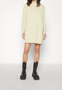 Gul huvtröja klänning med framfickor, ribbade manschetter och logodetalj. Matching med svarta kraftiga ankelstövlar.