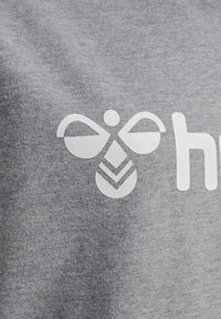 Grauer Stoff mit einem weißen Grafikdruck einer stilisierten Biene mit symmetrischen Flügeln und einem dreieckigen Muster darunter, neben dem Text "hey."
