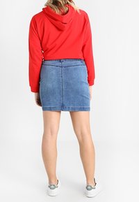 Felpa rossa con cappuccio, abbinata a una gonna di jeans blu. L'outfit è completato da sneakers bianche con dettagli verdi.