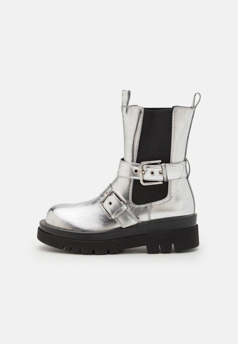 Srebrny metaliczny botek na kostkę z czarną elastyczną boczną panelą, masywną czarną podeszwą i paskiem z detalem klamry. Gładkie wykończenie.