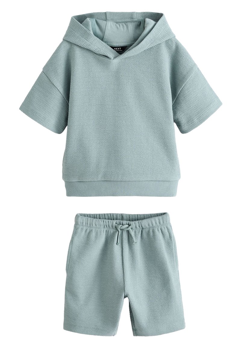 Helesinine tekstuuriga mugavuskomplekt, mis sisaldab lühikeste varrukatega kapuutsiga särki ja sobivaid lühikesi pükse, millel on elastne vöökoht ja nöör.