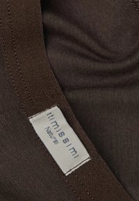 Brunt tyg med en slätt textur och en platt krage. En vit etikett som är sydd med "itmissimi" och "Natural" är synlig.