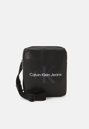 Bolso bandolera rectangular negro de Calvin Klein Jeans con correa ajustable y logotipo delantero sobre un fondo blanco liso.