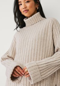 Beige gestreifter Pullover mit hohem Kragen und weiten Ärmeln. Hergestellt aus einem weichen, strukturierten Material, bietet er einen lässigen Schnitt und dicke Bündchen.