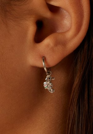 Zilveren hoepeloorbel met een zeepaardje charm, versierd met gekleurde accenten en kleine rhinestones, hangend uit de oorlel.