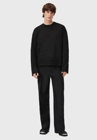 Czarny sweter o teksturowanej powierzchni z okrągłym dekoltem, w zestawieniu z luźnymi czarnymi spodniami. Ubranie ma długie rękawy oraz prosty krój.