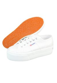 Baskets en toile blanches avec semelle plateforme, semelle en caoutchouc orange texturée, fermeture à lacets et détail de logo en relief sur le côté.