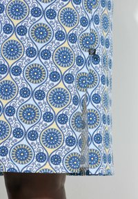 Falda con estampado floral en azul y amarillo con una abertura frontal, llevada sobre piel oscura.