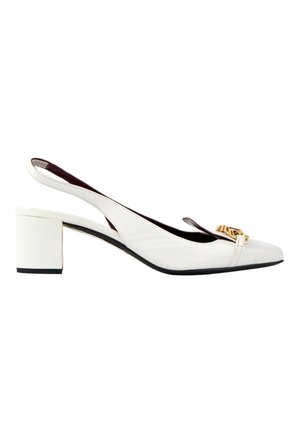 Hvid læder slingback pump med lav blokhæl og guldkædedetalje på spids tå mod hvid baggrund.