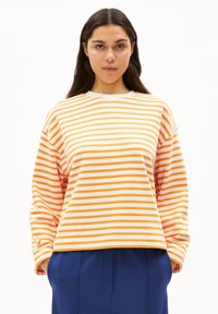 T-shirt a righe a maniche lunghe in bianco, arancione e giallo. Vestibilità ampia, scollatura rotonda e spalle scese, abbinata a pantaloni blu.