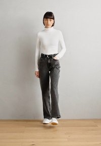 Bijela majica s dugim rukavima i izrezom na vratu uparena s tamnosivim širokim trapericama visokog struka. Model nosi bijele tenisice. Jednostavan, minimalistički stil.