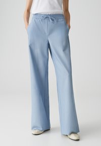 Pantalons large bleu clair avec taille à cordon, fabriqués à partir d'un tissu lisse ; dotés de deux poches latérales et d'une coupe décontractée.