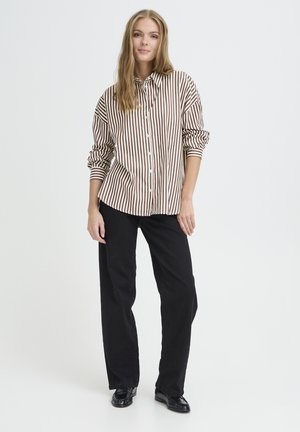 Gestreifte Button-Down-Bluse in Braun und Weiß, kombiniert mit schwarzen, weiten Hosen. Die Bluse hat aufgerollte Ärmel und einen klassischen Kragen.