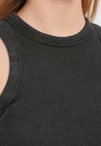 Black ribbed sleeveless top featuring a round neckline and textured fabric. No visible hardware or accents. Close-up view of material.