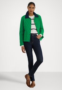 Grønn quiltet jakke med en marineblå krage, brukt over en hvit og marineblå stripete genser. Kombinert med mørke jeans og brune loafers.