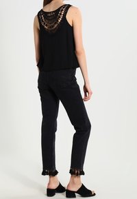 Czarny top bez rękawów z szczegółowym plecami wyhaftowanymi na szydełku, połączony z czarnymi spodniami z wysokim stanem na frędzlu oraz czarnymi butami slip-on.