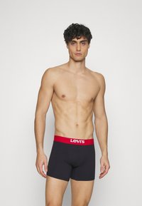 Svarta boxershorts med ett rött midjeband. Midjebandet har "Levi's"-logotypen i vitt. Tyget ser slätt och åtsittande ut.