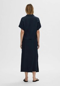 Dunkelbluse mit kurzen Ärmeln und Kragen, kombiniert mit einem langen, geraden Rock. Glattes Gewebe mit einem dezenten Glanz. Flache Sandalen.