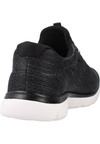 Chaussure de sport noire avec un dessus en tissu texturé, un col semblable à une chaussette et une semelle en caoutchouc blanche. Présente un design minimaliste et un talon renforcé.