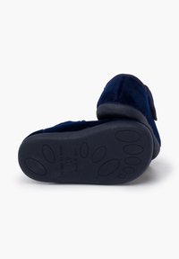 Zapatillas de ante azul con suela de goma plana; presentan una punta redondeada y un diseño texturizado en la parte inferior para mayor agarre. Fabricadas en España.