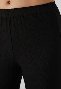 Black textured leggings featuring a flexible waistband, with a subtly rippled surface and a fitted design for comfort.