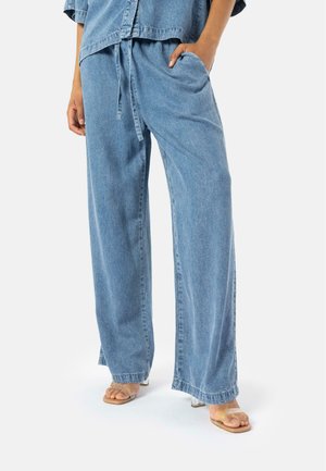 Light blue denim wide-leg pants with a drawstring waist, side pockets, and a relaxed fit, paired with clear strap sandals.