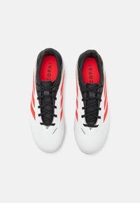 Botas de fútbol blancas con acentos negros, presentando detalles de rayas rojas, una superficie sintética suave y un diseño tradicional con cordones.