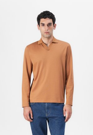 Langarm, V-hals shirt in een lichtbruine kleur, gemaakt van een zachte stof, gecombineerd met blauwe spijkerbroek. Eenvoudig, minimalistisch ontwerp.