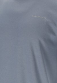 Lyseblåt stof med subtil struktur, med ordet "ENDURANCE" trykt med små store bogstaver nær øverste højre område.