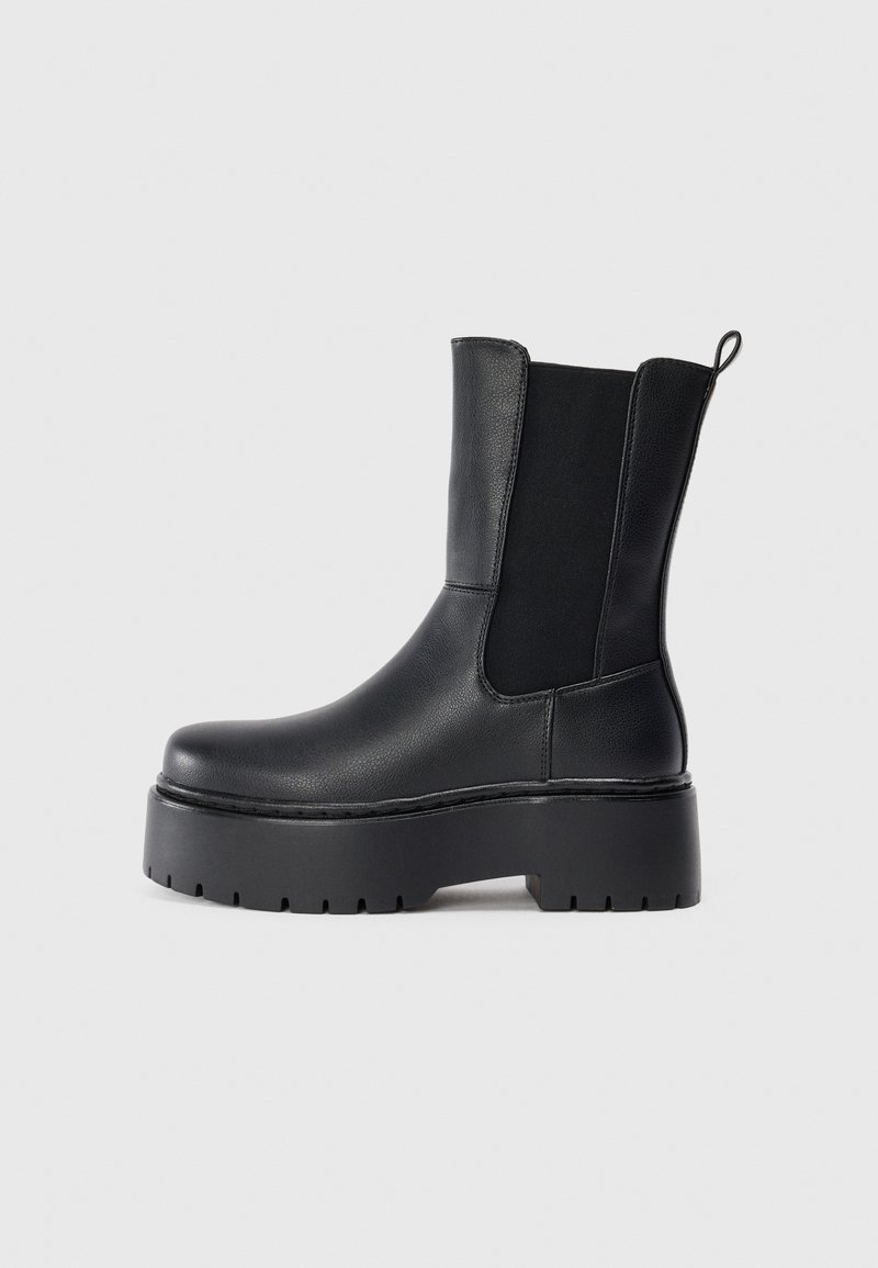 Botines negros hechos de cuero suave con paneles elásticos en los laterales y una suela de goma gruesa, que cuentan con una lengüeta en la parte posterior.