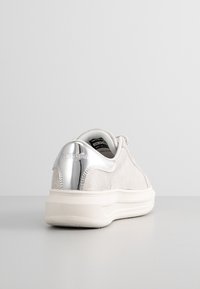 Ljust grå mockaskor med en silverdetalj på hälen, gummisula och minimalistisk design. Avslappnad stil som passar för vardagsbruk.