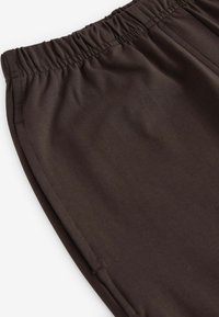 Bruine stoffen broek met een elastische tailleband, met een gladde textuur en gestikte naden, vanuit een schuine hoek weergegeven om de relaxte pasvorm te tonen.