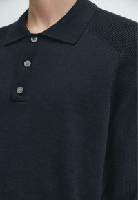 Polo blu navy con collo piatto, abbottonatura a tre pulsanti e dettagli testurizzati sulle spalle. Realizzato in tessuto a maglia costina.