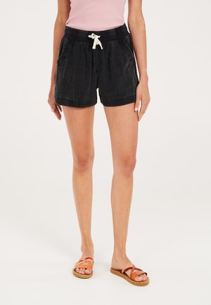 Shorts en coton noirs avec une taille élastique et un cordon de serrage, dotés de poches latérales et d'une coupe décontractée. Portés avec des sandales à lanières marron.