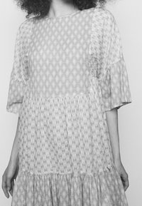 Lekka sukienka z mieszanką geometrycznych wzorów w jasnych odcieniach, z falbankowymi rękawami i warstwowym dołem z falbanami.